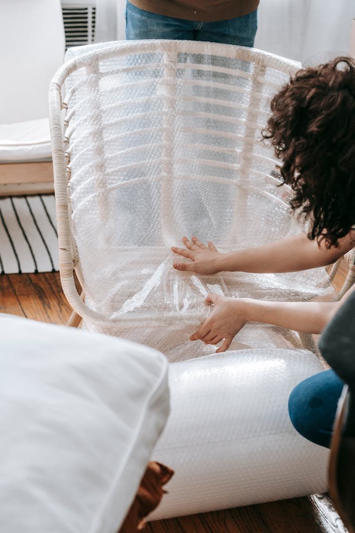 A woman carefully wraps a chair in bubble wrap to prepare for moving or relocation.
